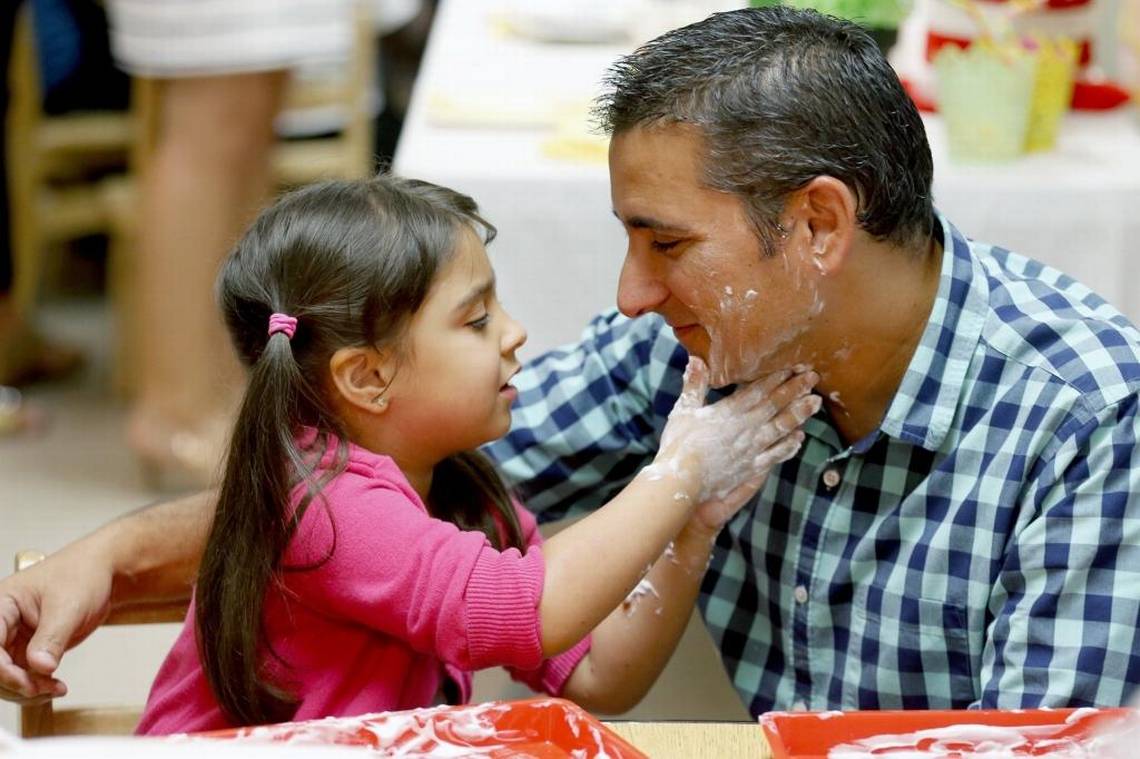 Little girl with pigtails  rubs shaving cream on her father’s face